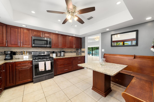 kitchen with stainless steel appliances, backsplash, a tray ceiling, ceiling fan, and light tile patterned floors