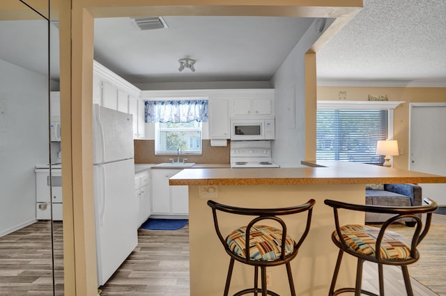 3647 SW Natura Ave Unit B, Deerfield Beach, FL 33441 - kitchen featuring white appliances, a kitchen bar, white cabinets, and light wood-type flooring