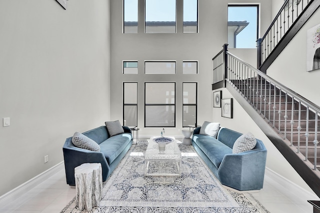 living room featuring stairs, baseboards, and a high ceiling