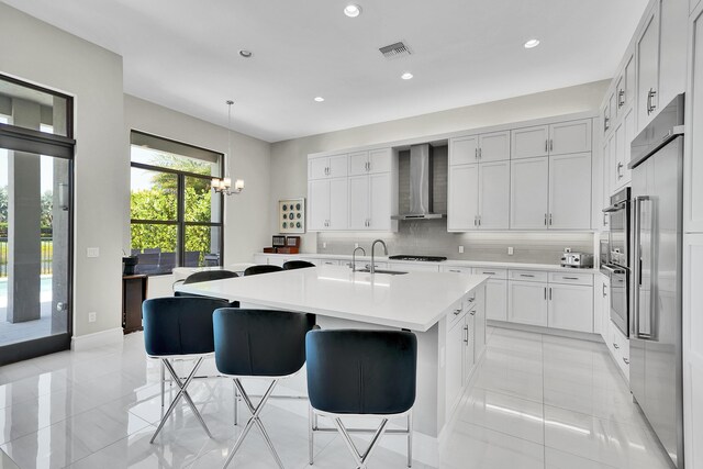 kitchen featuring wall chimney exhaust hood, light countertops, a chandelier, tasteful backsplash, and a kitchen bar