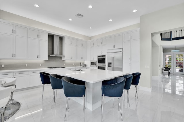 kitchen featuring built in appliances, wall chimney exhaust hood, a kitchen breakfast bar, light countertops, and recessed lighting
