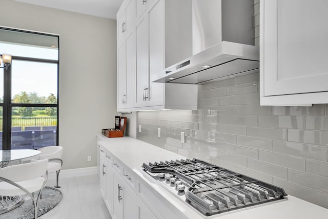 kitchen featuring wall chimney exhaust hood, stainless steel gas stovetop, light countertops, and white cabinets
