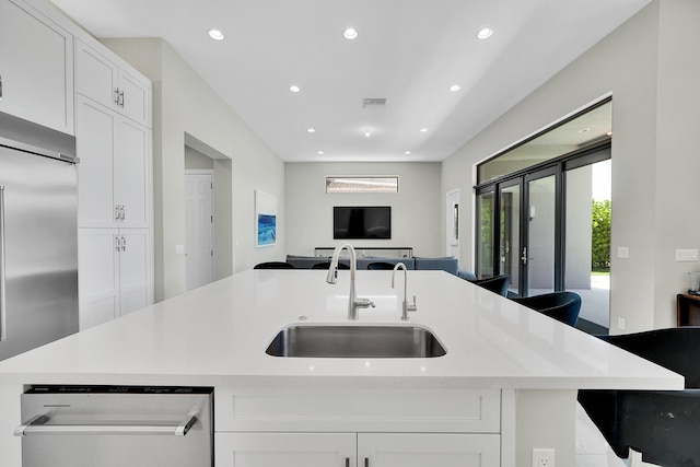 kitchen featuring a sink, built in refrigerator, open floor plan, a center island with sink, and white cabinetry
