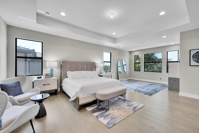 bedroom with a tray ceiling, light wood-style floors, recessed lighting, and baseboards