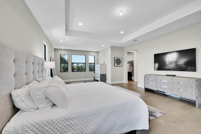 bedroom featuring wood finished floors, recessed lighting, baseboards, a raised ceiling, and a spacious closet