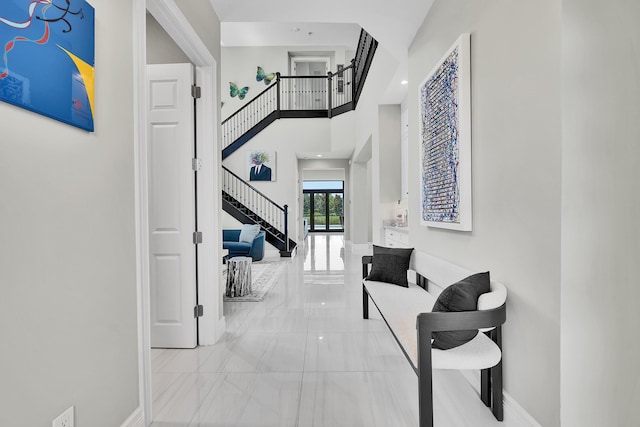 hallway with marble tiled floors, stairs, a towering ceiling, and baseboards