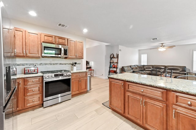 1184 Landings Run, Greenacres, FL 33413 - kitchen with appliances with stainless steel finishes, open floor plan, ceiling fan, light stone counters, and brown cabinetry
