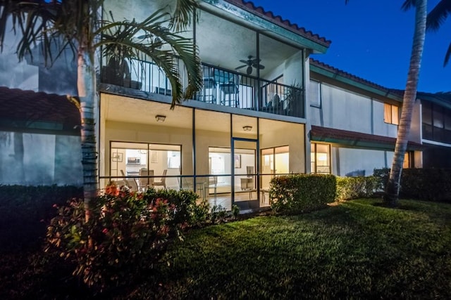 6 E Lexington Ln Unit C, Palm Beach Gardens, FL 33418 - back of house at night with a balcony, ceiling fan, stucco siding, a tiled roof, and a yard
