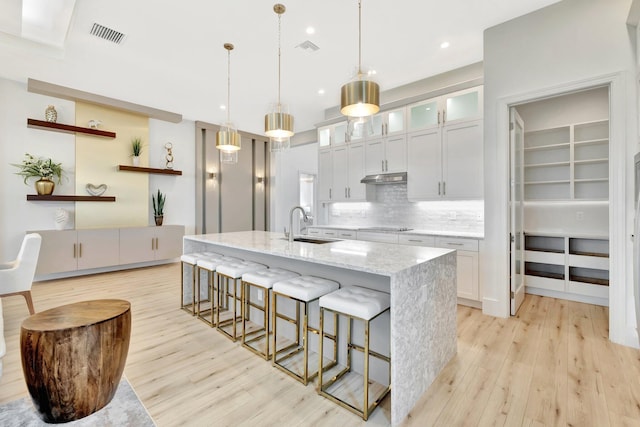17135 SW Ambrose Way, Port Saint Lucie, FL 34986 - kitchen with light wood-style floors, under cabinet range hood, a kitchen bar, a center island with sink, and tasteful backsplash
