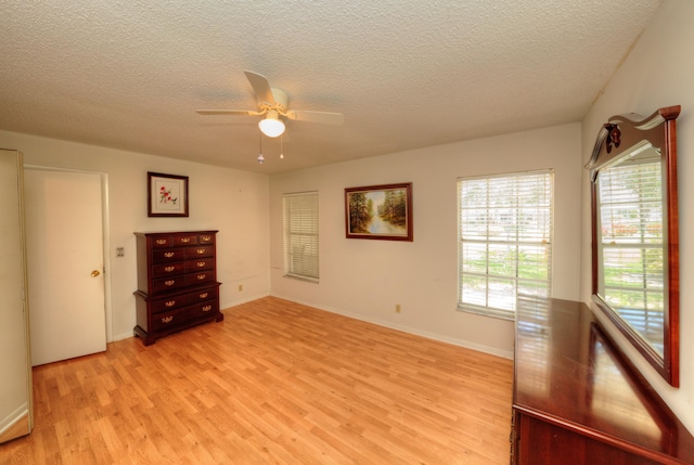 unfurnished room with light wood finished floors, a textured ceiling, healthy amount of natural light, a ceiling fan, and baseboards