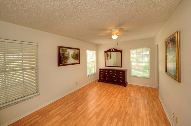 unfurnished room with light wood-style flooring, plenty of natural light, ceiling fan, a textured ceiling, and baseboards