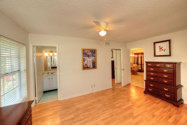 bedroom with light wood finished floors, a sink, ensuite bath, a textured ceiling, and a ceiling fan