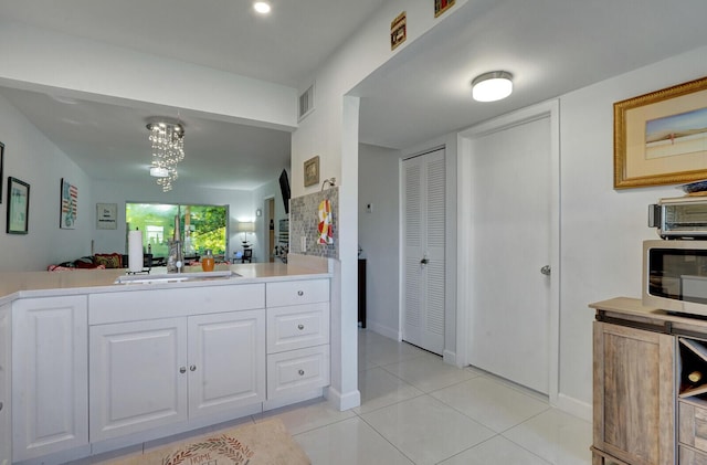 130 Lake Meryl Dr Unit 226, West Palm Beach, FL 33411 - kitchen featuring light countertops, light tile patterned floors, white cabinets, stainless steel microwave, and a chandelier