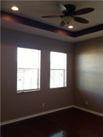 empty room featuring dark wood finished floors, baseboards, healthy amount of natural light, a raised ceiling, and recessed lighting