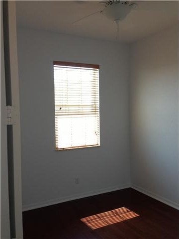 empty room with dark wood-type flooring, a ceiling fan, and baseboards