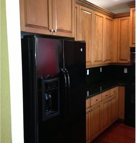 kitchen with black refrigerator with ice dispenser, dark stone counters, dark wood-type flooring, and brown cabinetry
