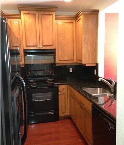 kitchen featuring black appliances, a sink, under cabinet range hood, wood finished floors, and dark stone counters