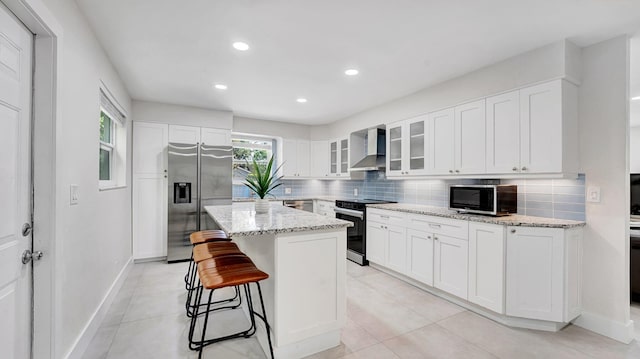 218 NE 10th St, Delray Beach, FL 33444 - kitchen featuring stainless steel appliances, wall chimney range hood, a kitchen bar, tasteful backsplash, and glass insert cabinets