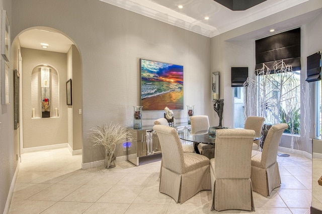 dining space featuring arched walkways, light tile patterned floors, baseboards, a textured wall, and ornamental molding