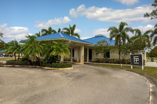 ranch-style home with a standing seam roof, metal roof, stucco siding, and asphalt driveway