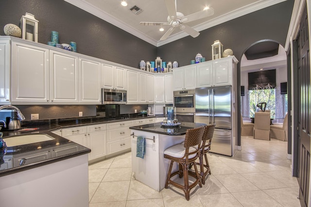 kitchen with appliances with stainless steel finishes, a sink, ornamental molding, white cabinetry, and light tile patterned floors