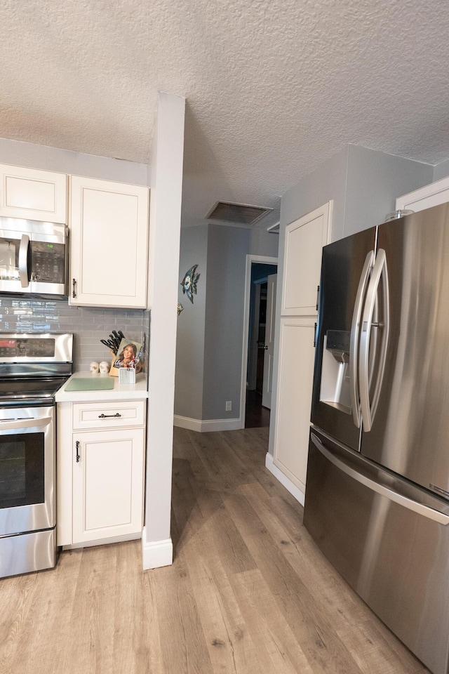 1325 Strawberry Ln, West Palm Beach, FL 33415 - kitchen with appliances with stainless steel finishes, light wood-type flooring, white cabinetry, tasteful backsplash, and a textured ceiling