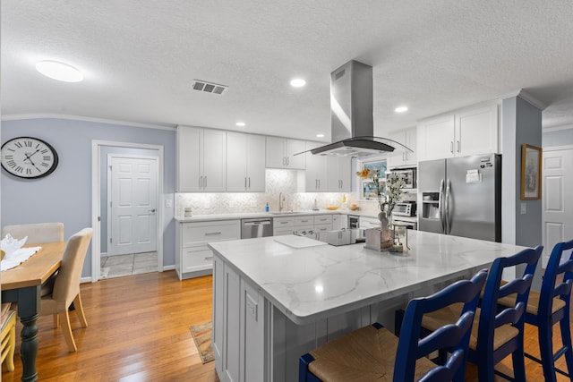 454 Tequesta Dr, Tequesta, FL 33469 - kitchen featuring stainless steel appliances, island range hood, crown molding, a kitchen bar, and light wood-type flooring