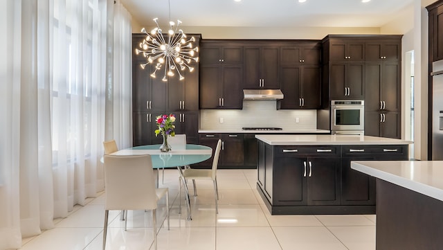 8520 Lewis River Rd, Delray Beach, FL 33446 - kitchen with stainless steel oven, under cabinet range hood, light countertops, a chandelier, and cooktop