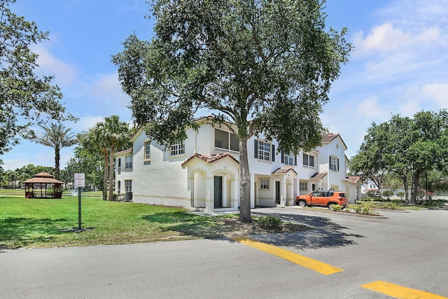 174 SE Kitching Cir Unit 174, Stuart, FL 34994 - view of front of home with uncovered parking, a gazebo, stucco siding, and a front yard