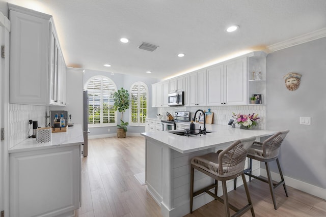 kitchen featuring stainless steel appliances, a sink, white cabinets, tasteful backsplash, and a breakfast bar area