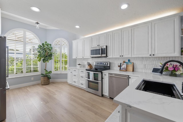kitchen with appliances with stainless steel finishes, a sink, baseboards, backsplash, and recessed lighting