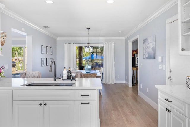 kitchen with a sink, white cabinets, ornamental molding, baseboards, and light wood-type flooring
