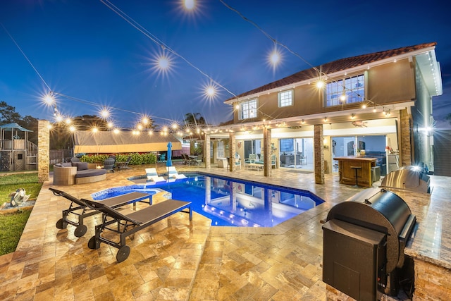 pool at night featuring area for grilling, exterior bar, and a patio