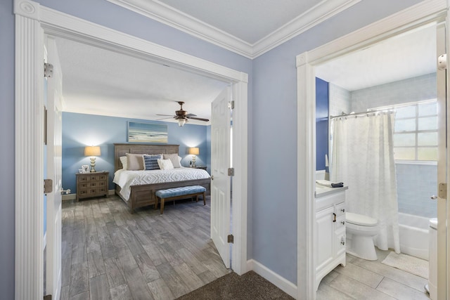 bedroom featuring crown molding, light wood-style floors, ensuite bath, a ceiling fan, and baseboards