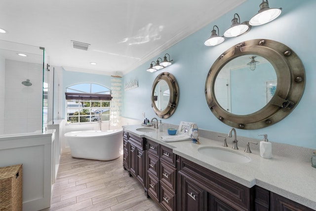 full bathroom featuring crown molding, wood finished floors, a freestanding tub, double vanity, and tiled shower