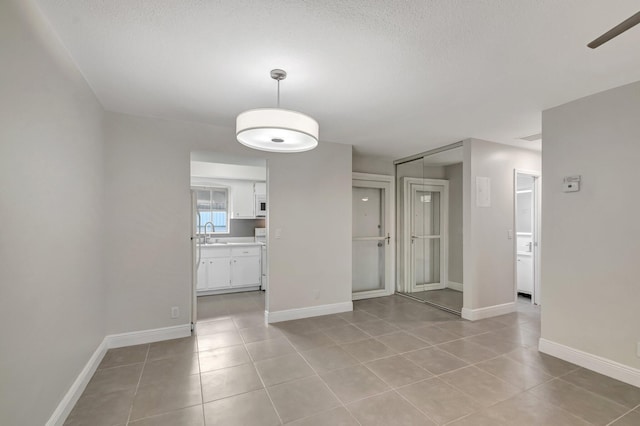 spare room with light tile patterned floors, a sink, baseboards, ceiling fan, and a textured ceiling