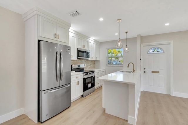 kitchen with appliances with stainless steel finishes, a sink, light wood-type flooring, decorative backsplash, and white cabinets