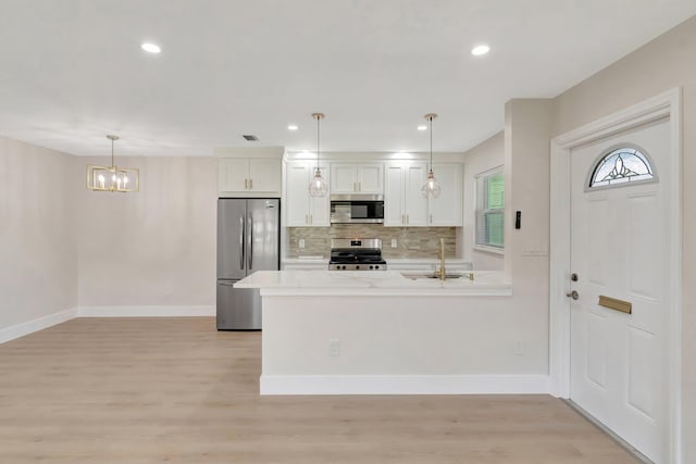 kitchen with appliances with stainless steel finishes, a chandelier, decorative backsplash, baseboards, and light wood-type flooring