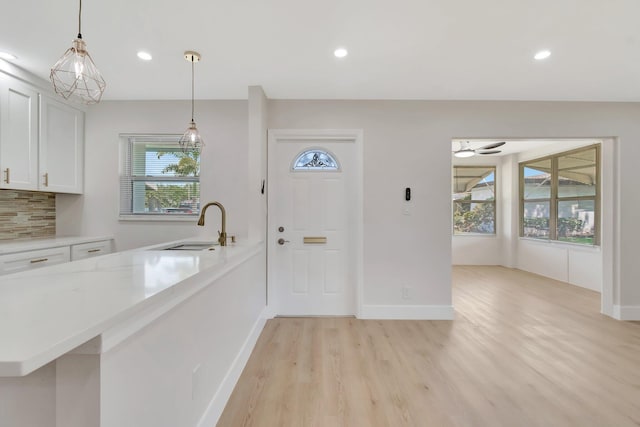 kitchen with a sink, light wood finished floors, white cabinets, pendant lighting, and recessed lighting
