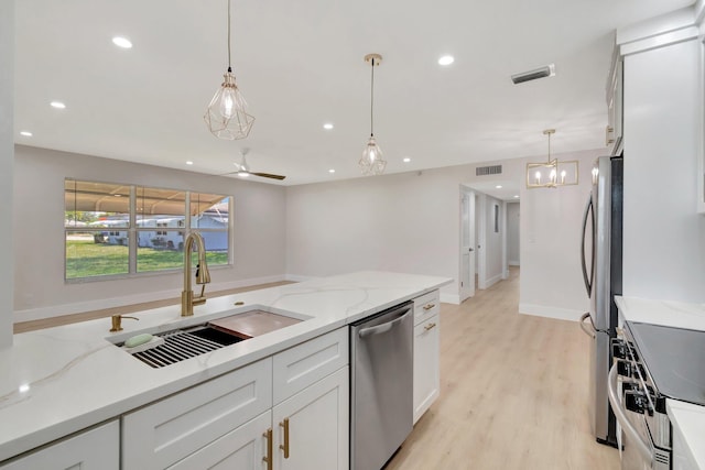 kitchen featuring stainless steel appliances, a sink, light stone counters, pendant lighting, and white cabinets