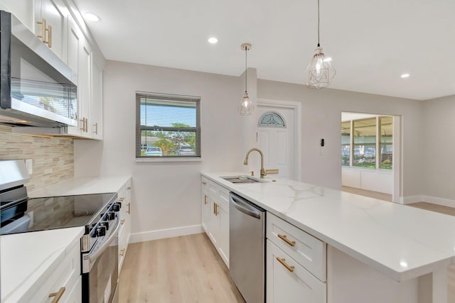 kitchen featuring stainless steel appliances, a sink, a peninsula, decorative backsplash, and light wood-type flooring