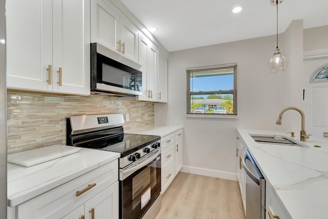 kitchen featuring appliances with stainless steel finishes, a sink, backsplash, baseboards, and light wood-style floors