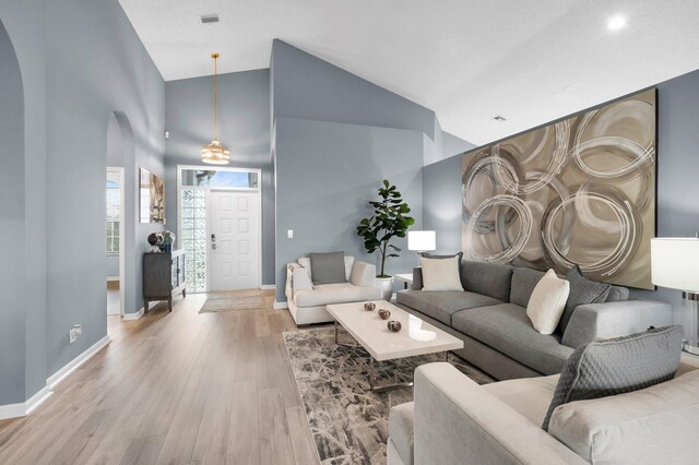 10393 Lexington Cir S, Boynton Beach, FL 33436 - living room featuring arched walkways, light wood finished floors, baseboards, and high vaulted ceiling