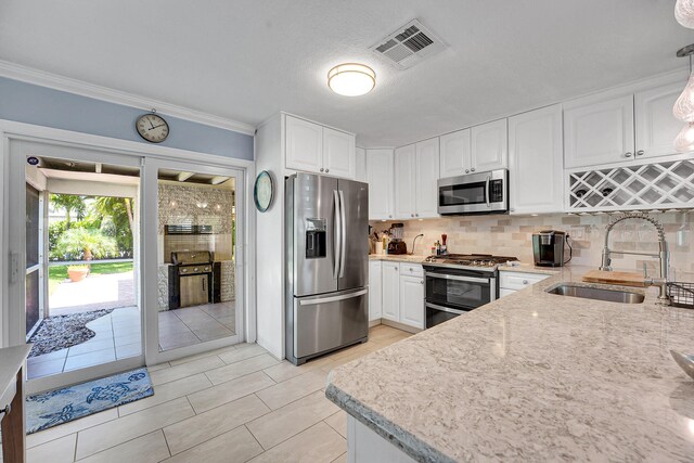 kitchen with stainless steel appliances, a sink, white cabinetry, tasteful backsplash, and ornamental molding