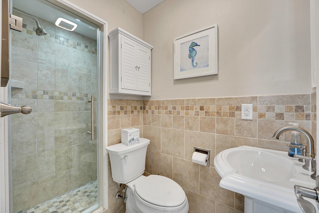 bathroom with a shower stall, a sink, toilet, tile walls, and wainscoting
