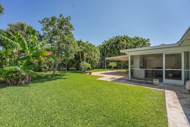 view of grassy yard with a sunroom, a patio area, and ceiling fan