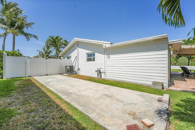 view of side of home with a gate, a patio, central AC, and stucco siding