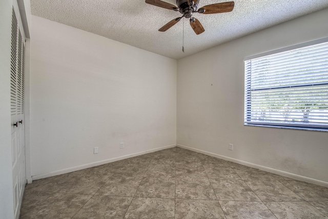 empty room with a textured ceiling, a ceiling fan, and baseboards