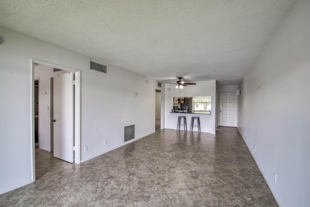 unfurnished living room with ceiling fan, a textured ceiling, and baseboards