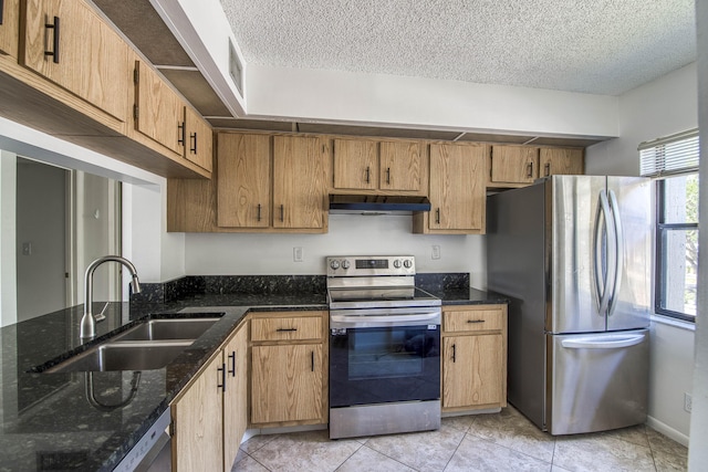 kitchen with stainless steel appliances, under cabinet range hood, a sink, a textured ceiling, and dark stone counters